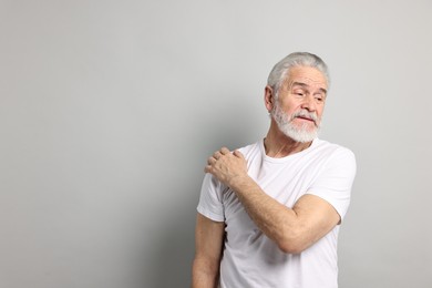 Arthritis symptoms. Man suffering from pain in shoulder on gray background, space for text