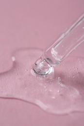 Photo of Dripping cosmetic serum from pipette onto pink background, macro view