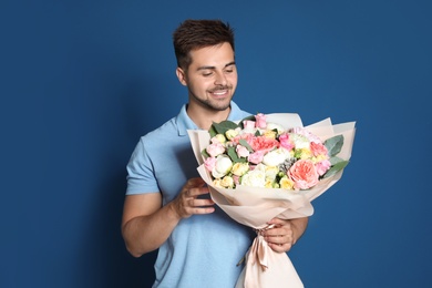 Young handsome man with beautiful flower bouquet on blue background