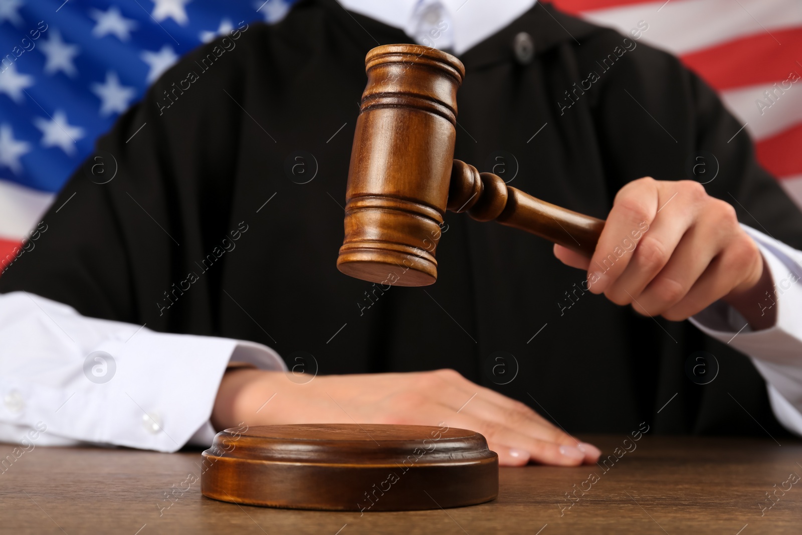 Photo of Judge with gavel at wooden table against flag of United States, closeup