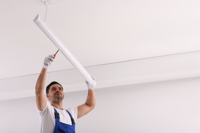 Ceiling light. Electrician installing led linear lamp indoors, low angle view. Space for text