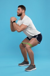 Photo of Young man exercising with elastic resistance band on light blue background