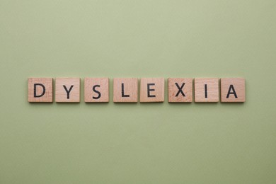 Photo of Wooden tiles with word Dyslexia on olive background, flat lay