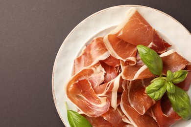Photo of Slices of tasty cured ham and basil on grey background, top view. Space for text