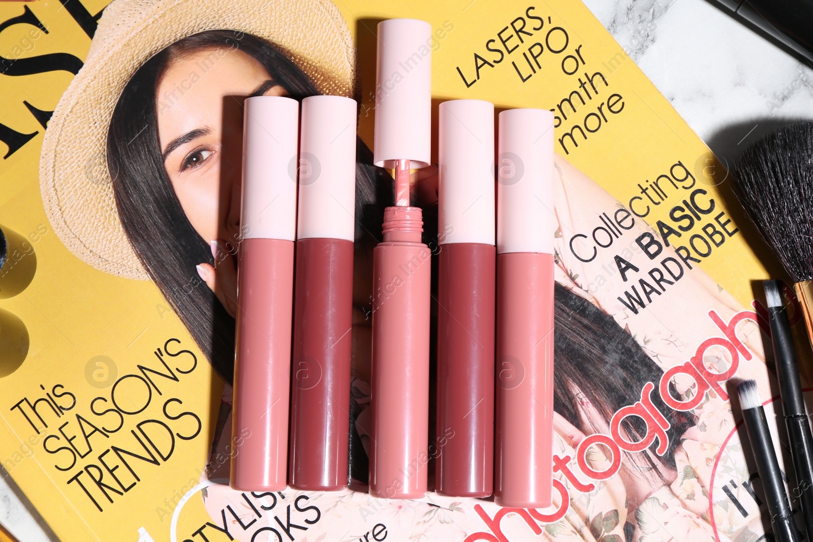 Photo of Bright lip glosses and fashion magazine on table, flat lay