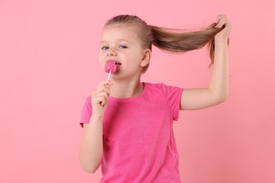 Photo of Cute little girl licking lollipop on pink background