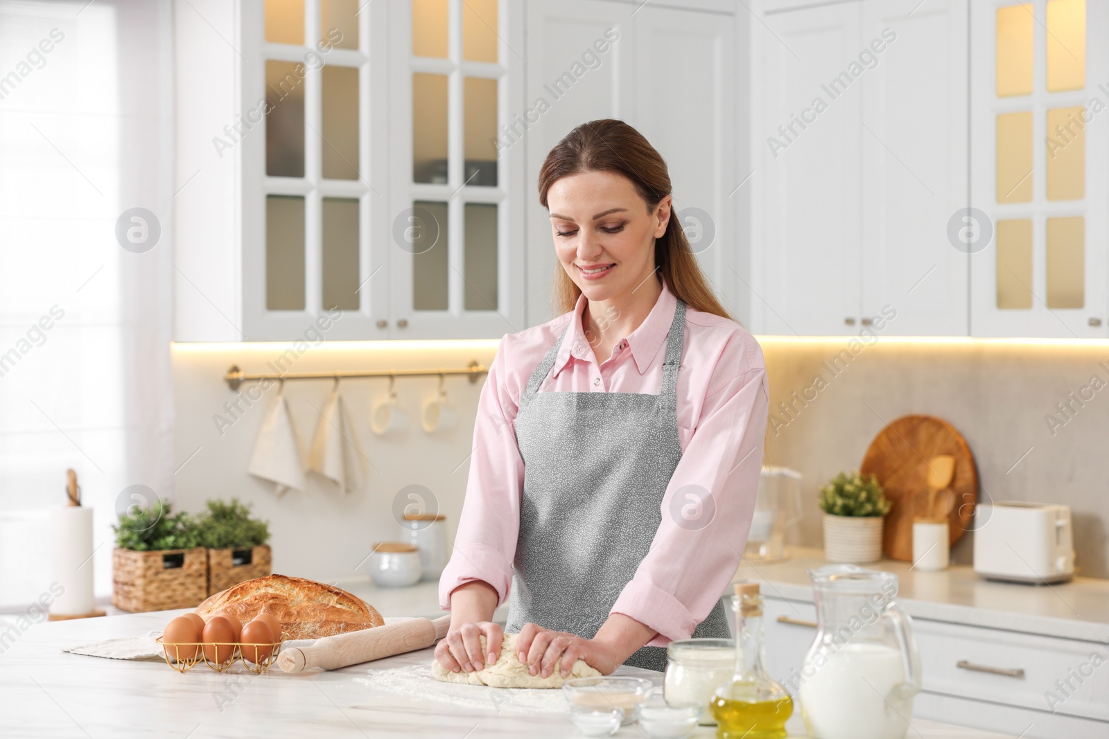 Photo of Making bread. Woman kneading dough at white table in kitchen