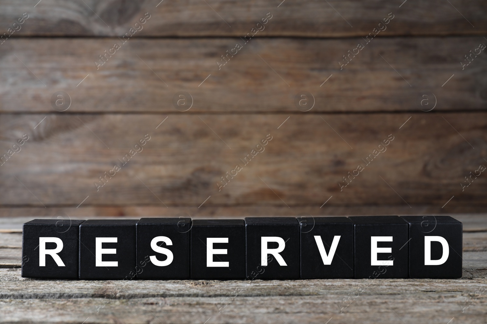 Photo of Word RESERVED made with cubes on wooden surface. Table setting element