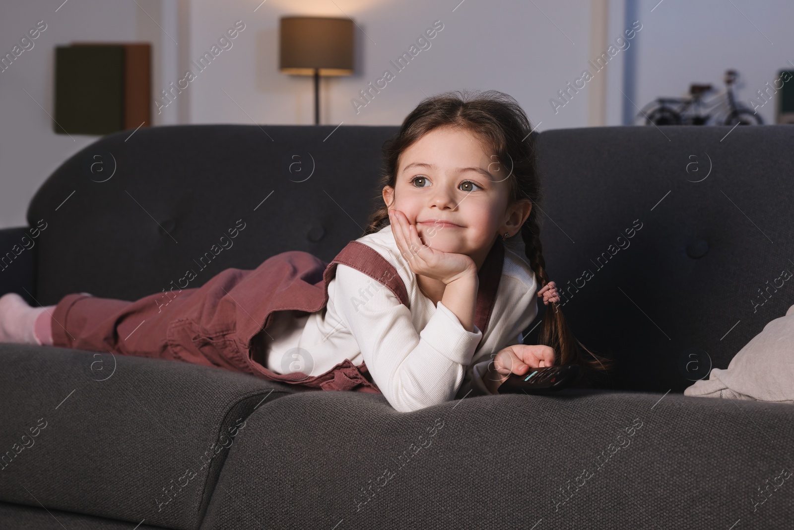 Photo of Cute little girl watching TV on sofa at home