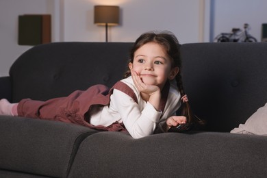 Photo of Cute little girl watching TV on sofa at home
