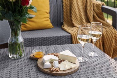 Photo of Vase with roses, glasses of wine and snacks on rattan table at balcony