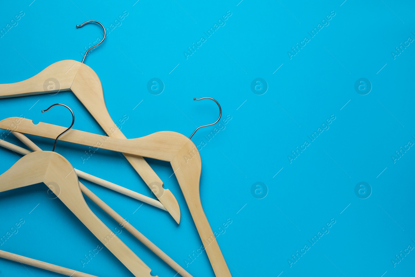 Photo of Empty wooden hangers on light blue background, flat lay. Space for text