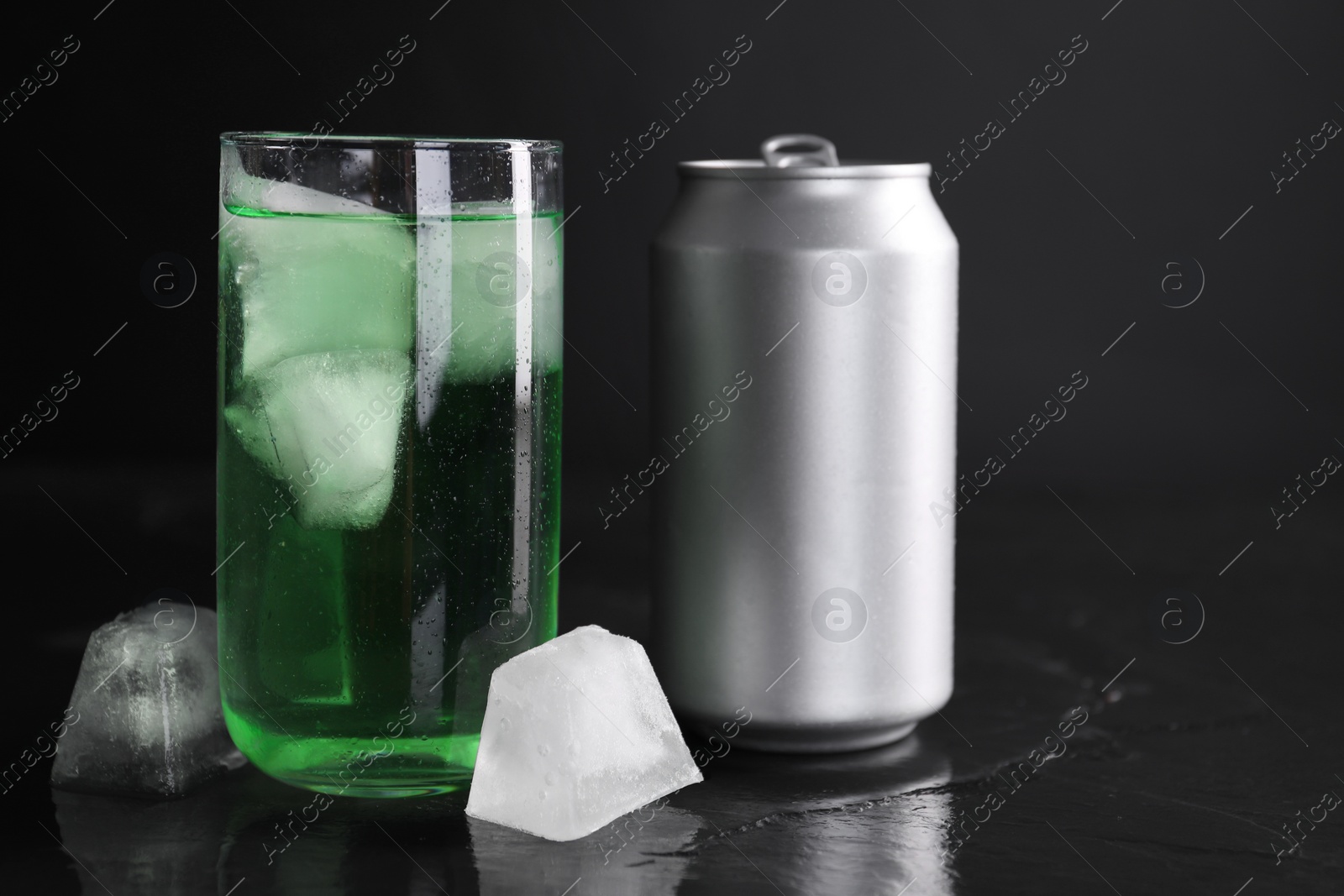 Photo of Tasty energy drink with ice cubes in glass and aluminium can on black table, closeup