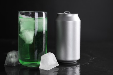 Photo of Tasty energy drink with ice cubes in glass and aluminium can on black table, closeup