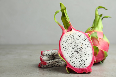 Photo of Delicious cut and whole dragon fruits (pitahaya) on grey table. Space for text