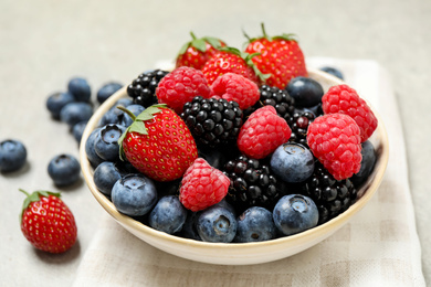 Mix of different fresh berries in bowl on light grey table