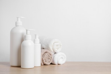Bottles of cosmetic products and rolled towels on wooden table. Space for text