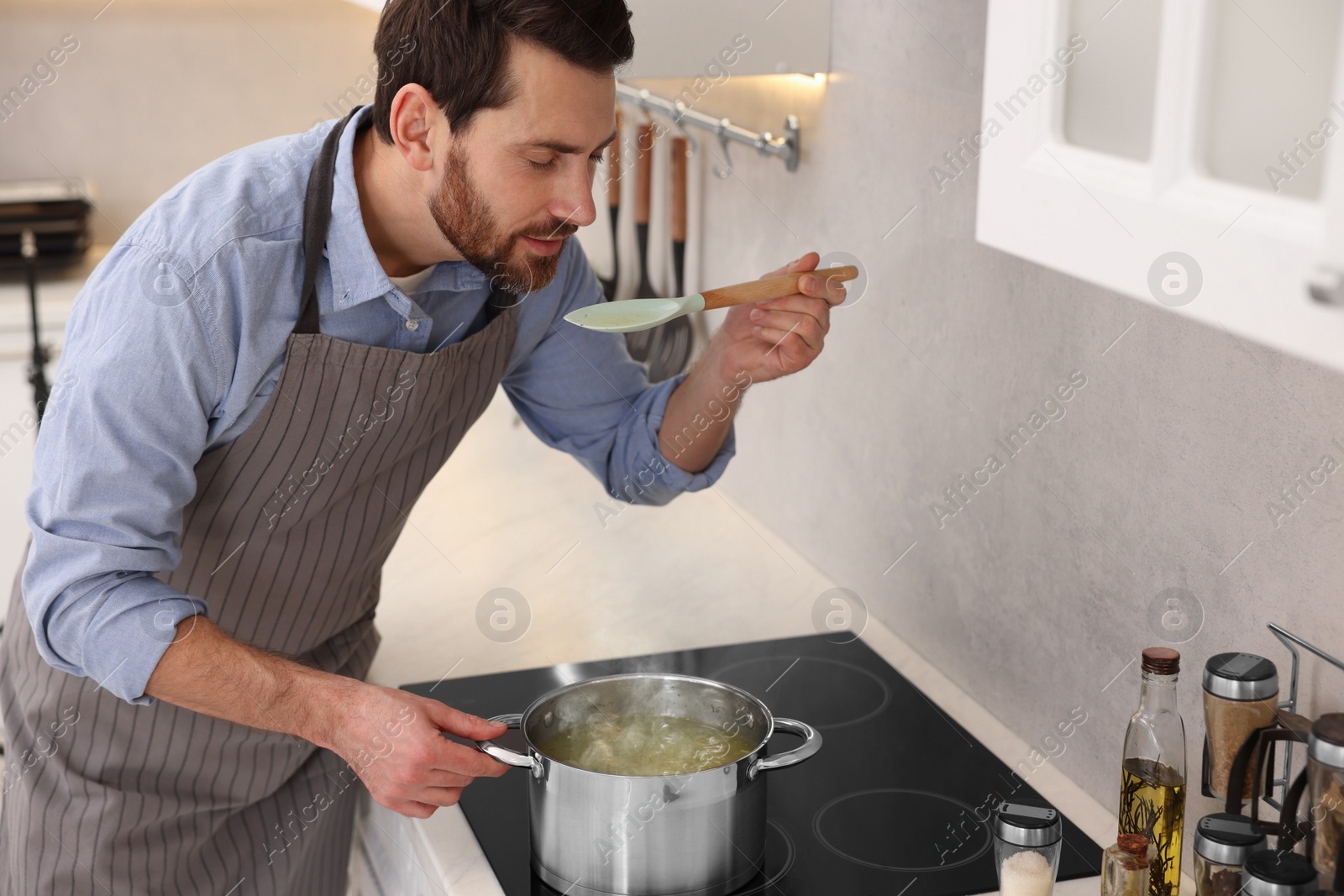 Photo of Man tasting delicious chicken soup in kitchen