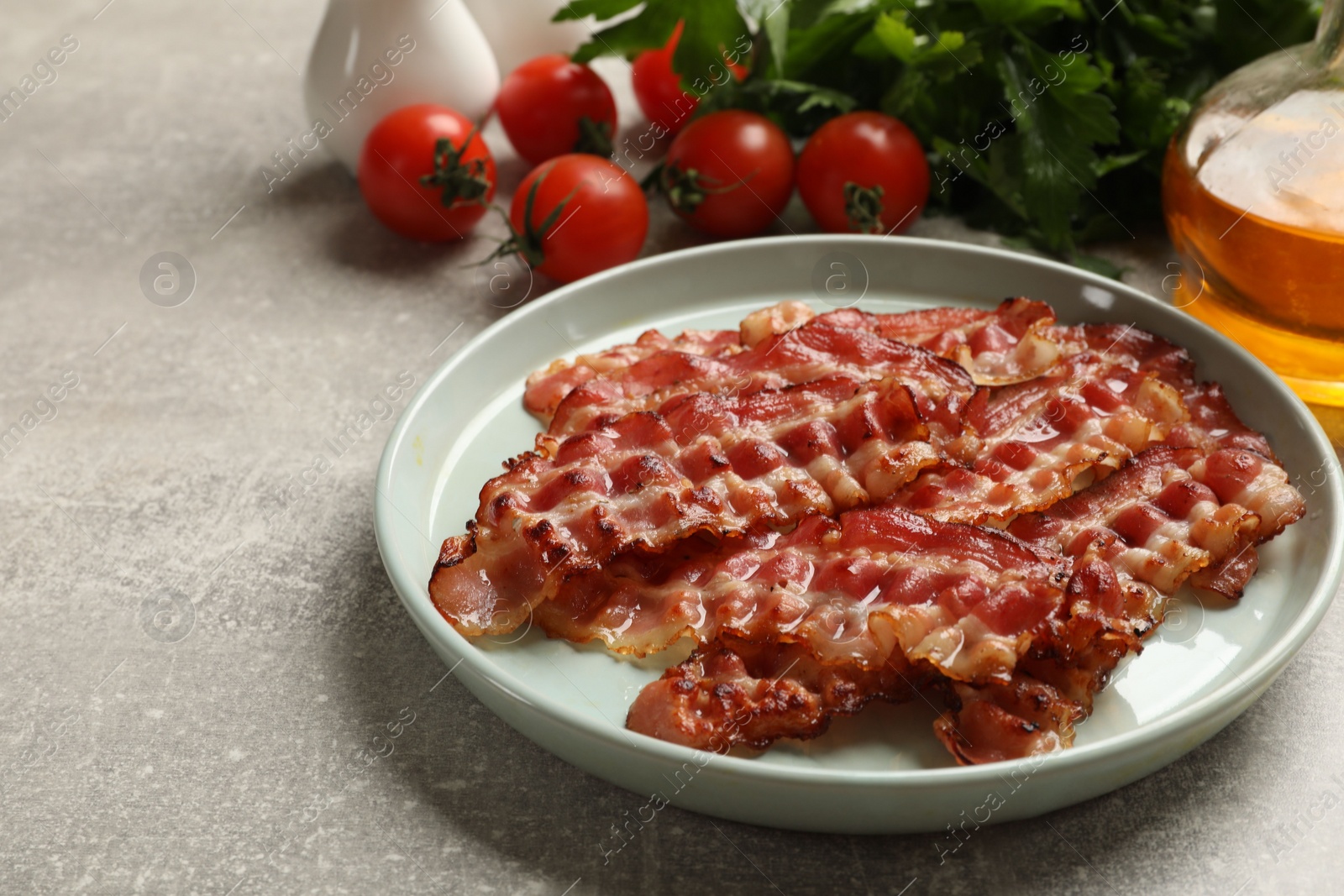 Photo of Plate with fried bacon slices, tomatoes and parsley on grey textured table, closeup