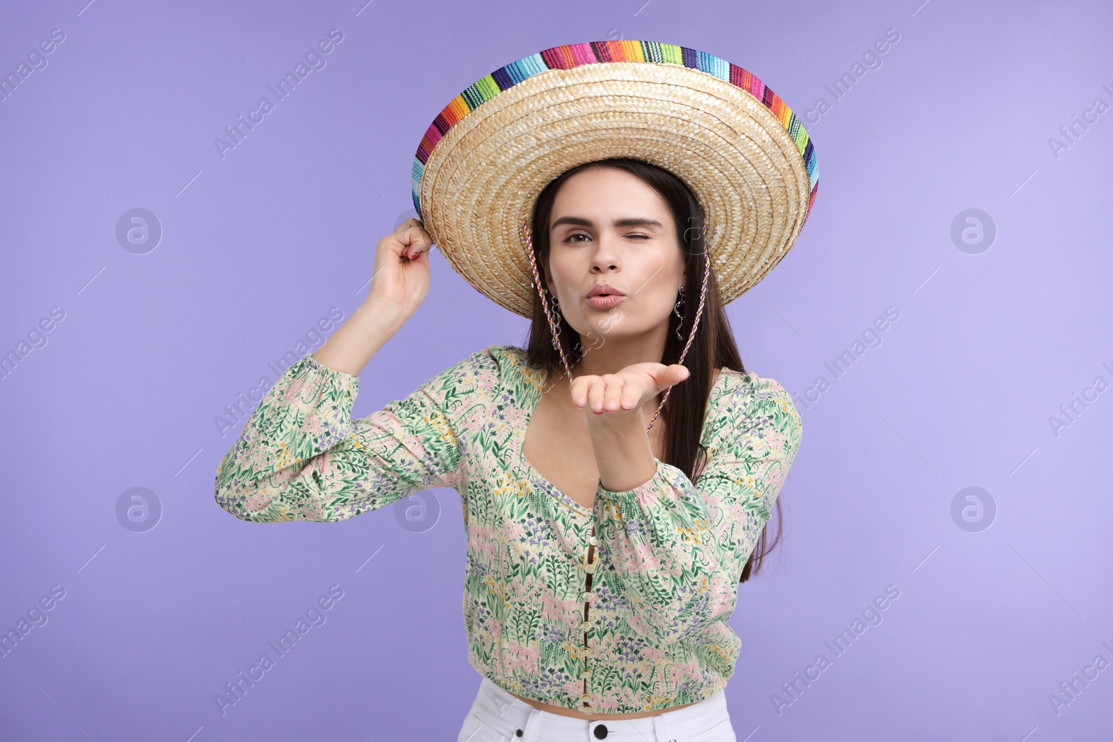 Photo of Young woman in Mexican sombrero hat blowing kiss on violet background