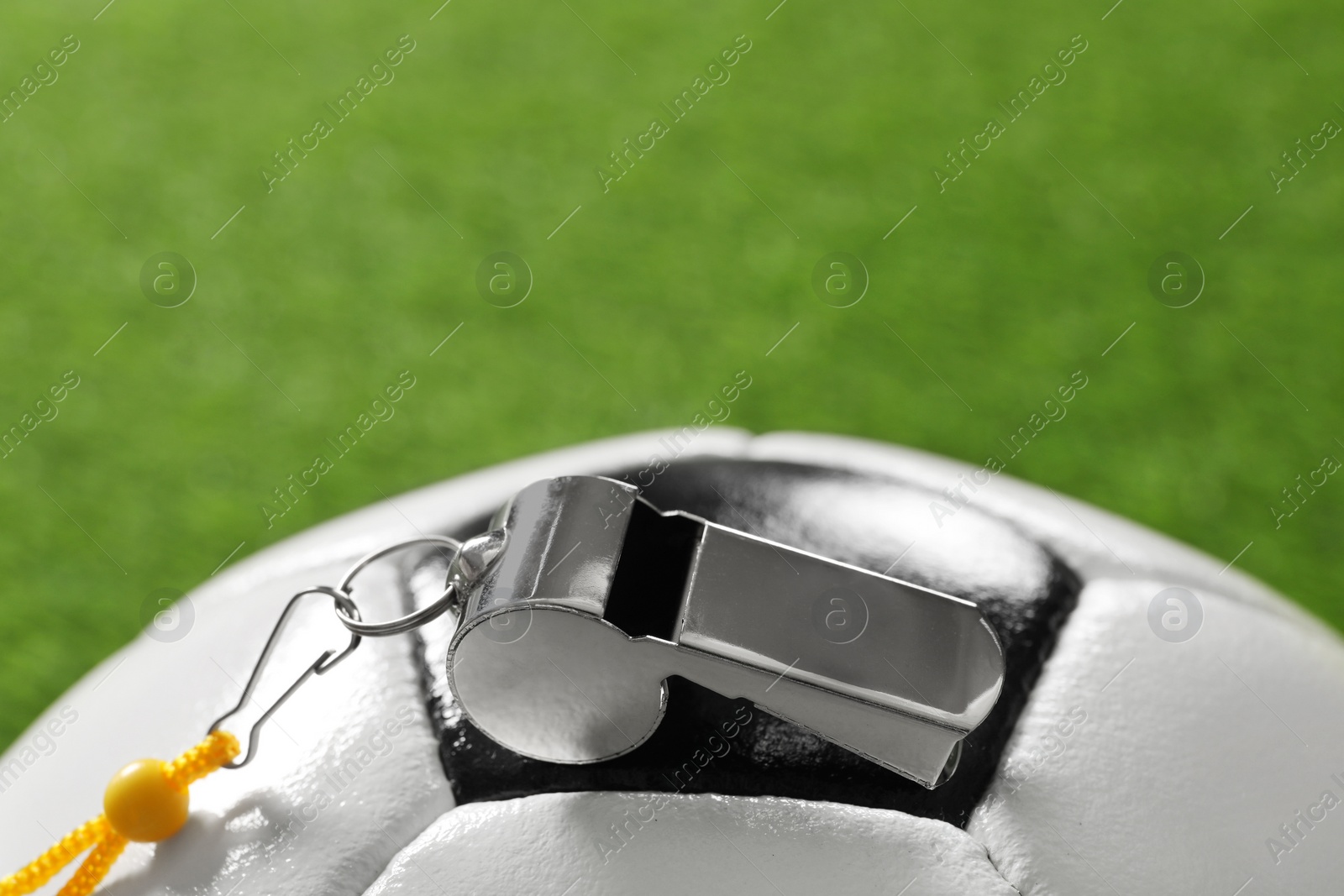 Photo of Football referee equipment. Soccer ball and metal whistle on green grass, closeup with space for text