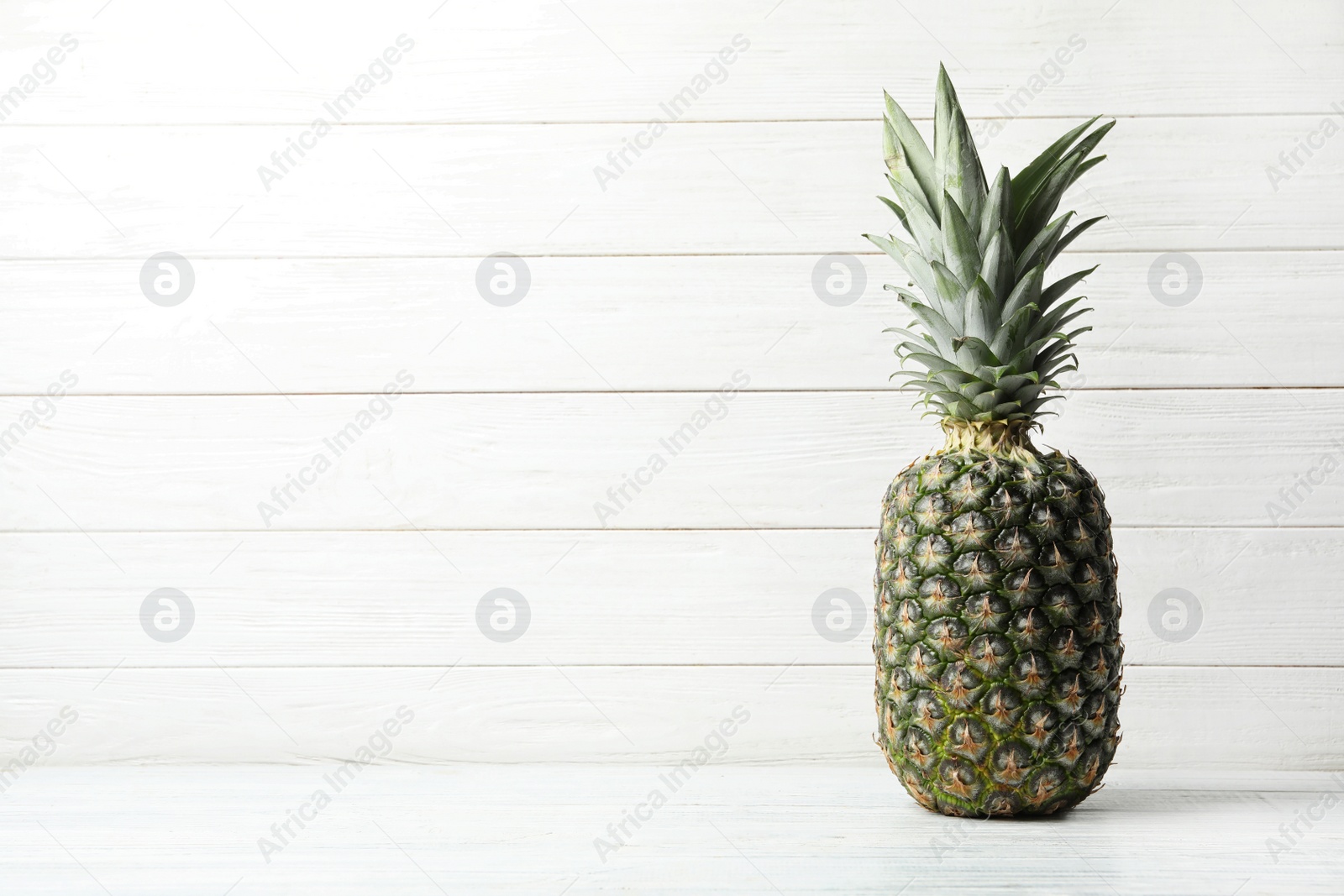 Photo of Fresh delicious pineapple on table against wooden background, space for text