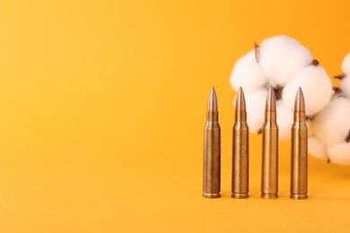 Photo of Bullets and beautiful fluffy cotton flowers on yellow background, space for text