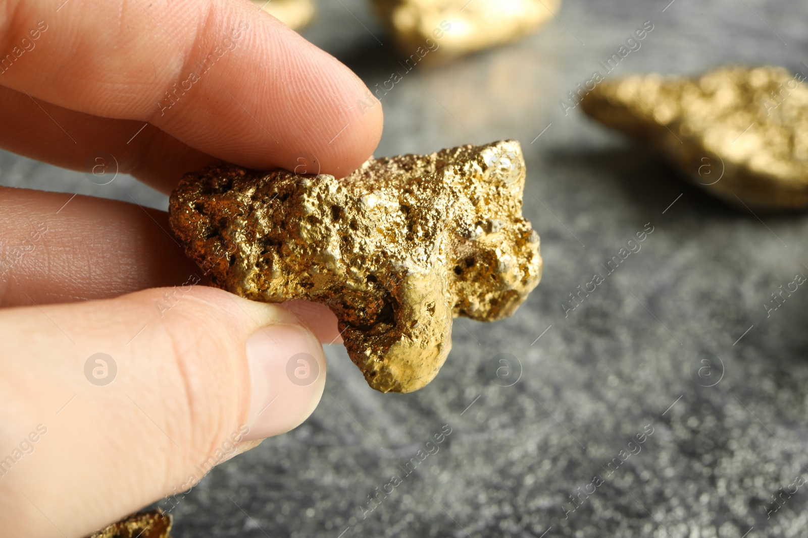 Photo of Woman holding gold nugget at grey textured table, closeup. Space for text