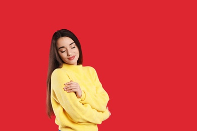 Beautiful young woman wearing yellow warm sweater on red background. Space for text