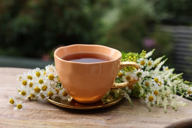 Photo of Cup of delicious chamomile tea and fresh flowers outdoors