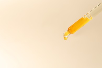 Dripping cosmetic serum from pipette on beige background, closeup. Space for text