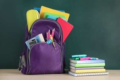 Photo of Color backpack and stationery on table near chalkboard with space for text. Ready for school