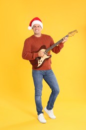 Photo of Man in Santa hat playing electric guitar on yellow background. Christmas music