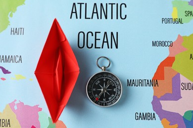 Photo of Red paper boat and compass on world map, flat lay