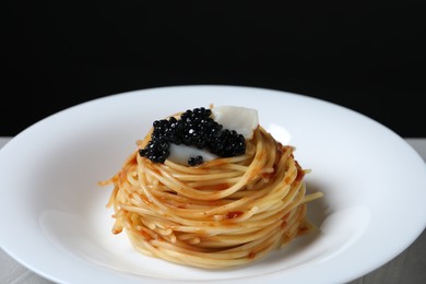 Photo of Tasty spaghetti with tomato sauce and black caviar on plate against dark background, closeup. Exquisite presentation of pasta dish