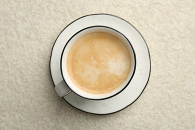 Photo of Tasty cappuccino in cup and saucer on light textured table, top view