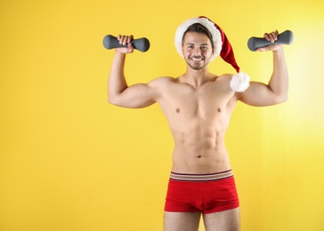 Shirtless sexy young Santa Claus with dumbbells on color background