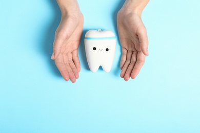 Photo of Woman holding hands near model of tooth with cute face on color background, top view. Space for text