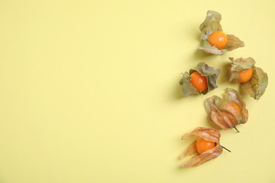 Photo of Ripe physalis fruits with dry husk on yellow background, flat lay. Space for text
