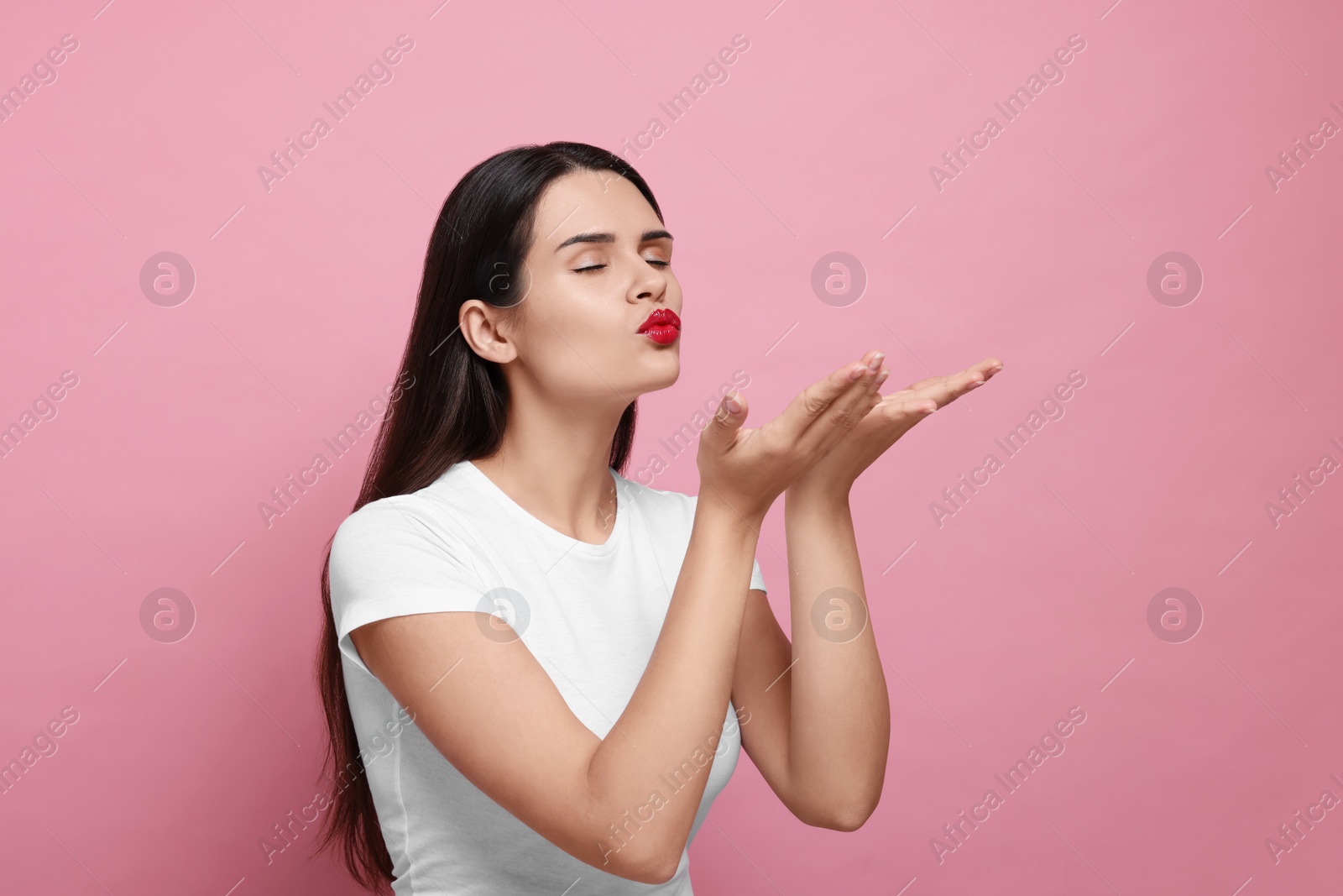 Photo of Beautiful young woman blowing kiss on pink background. Space for text
