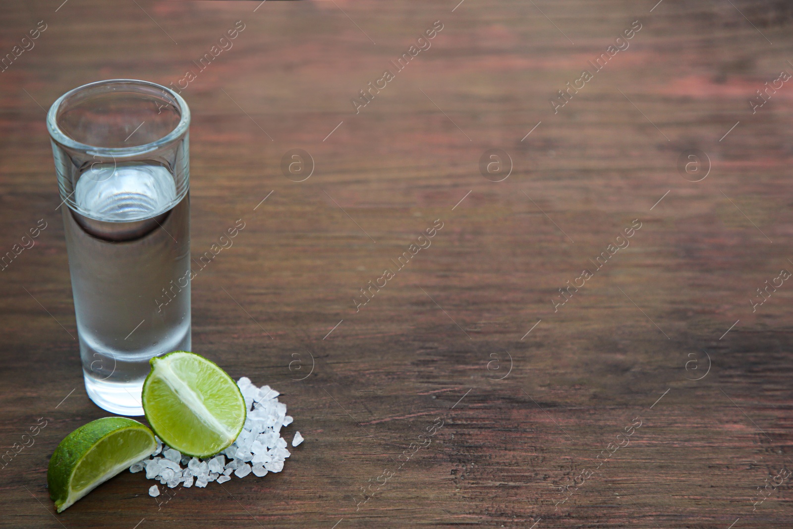 Photo of Mexican tequila shot with lime slices and salt on wooden table, space for text. Drink made from agave