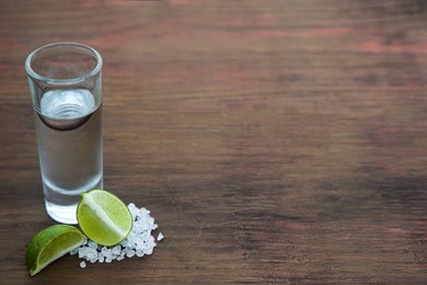 Photo of Mexican tequila shot with lime slices and salt on wooden table, space for text. Drink made from agave