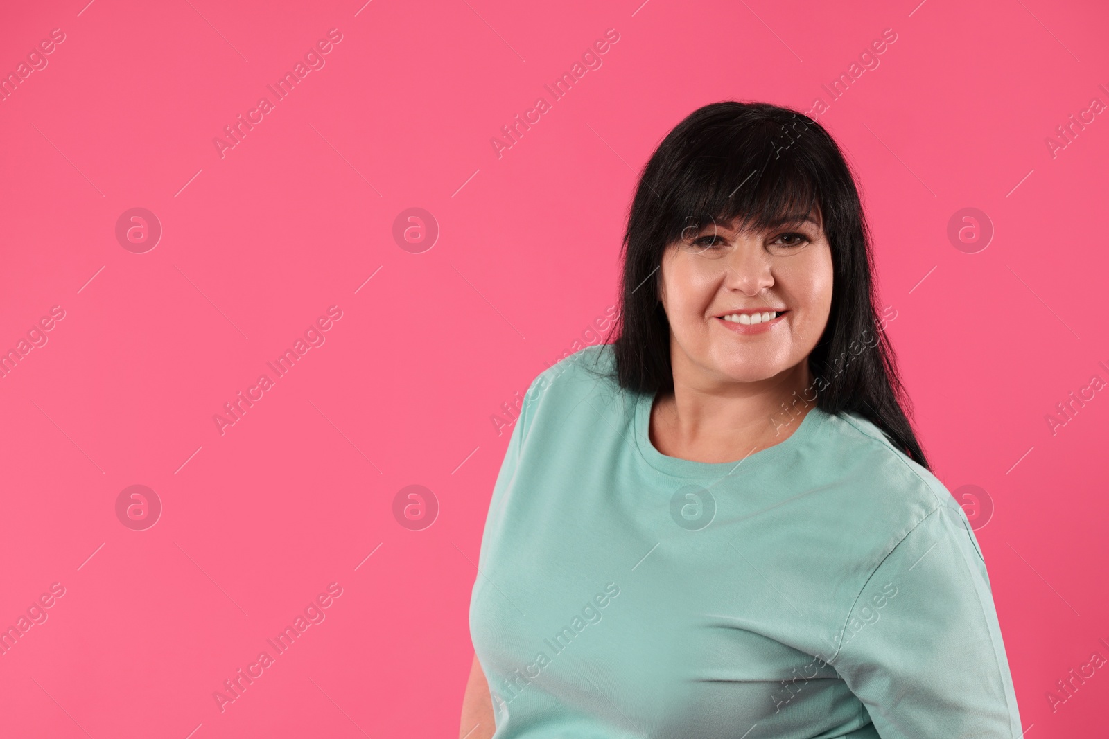 Photo of Beautiful overweight mature woman with charming smile on pink background. Space for text