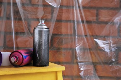 Photo of Used cans of spray paints on table near brick wall indoors, space for text. Graffiti supplies