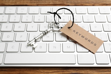 Photo of Keyboard, vintage key and tag with word KEYWORDS on wooden table, closeup