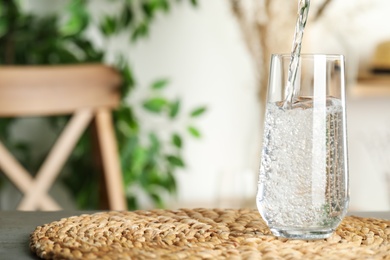 Photo of Pouring water into glass on table indoors, space for text. Refreshing drink