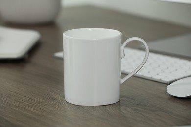 Photo of White ceramic mug on wooden table at workplace. Mockup for design