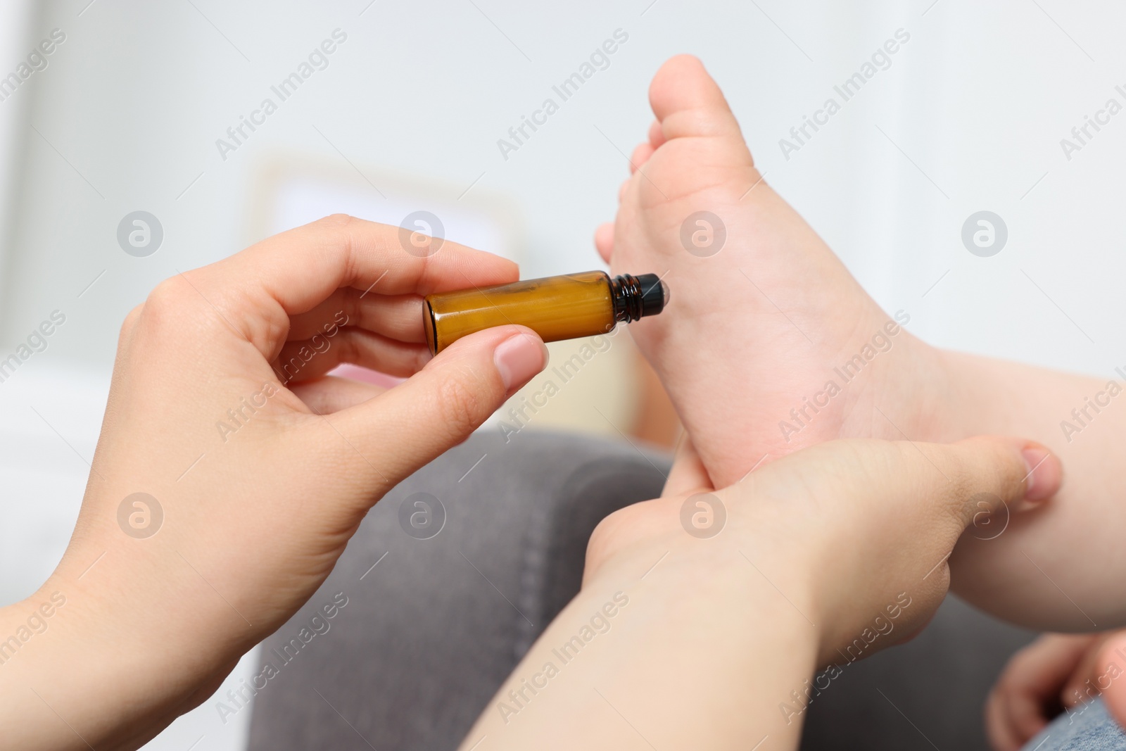 Photo of Mother applying essential oil from roller bottle onto her baby`s heel indoors, closeup