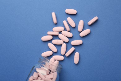 Bottle of pink vitamin capsules on blue background, top view