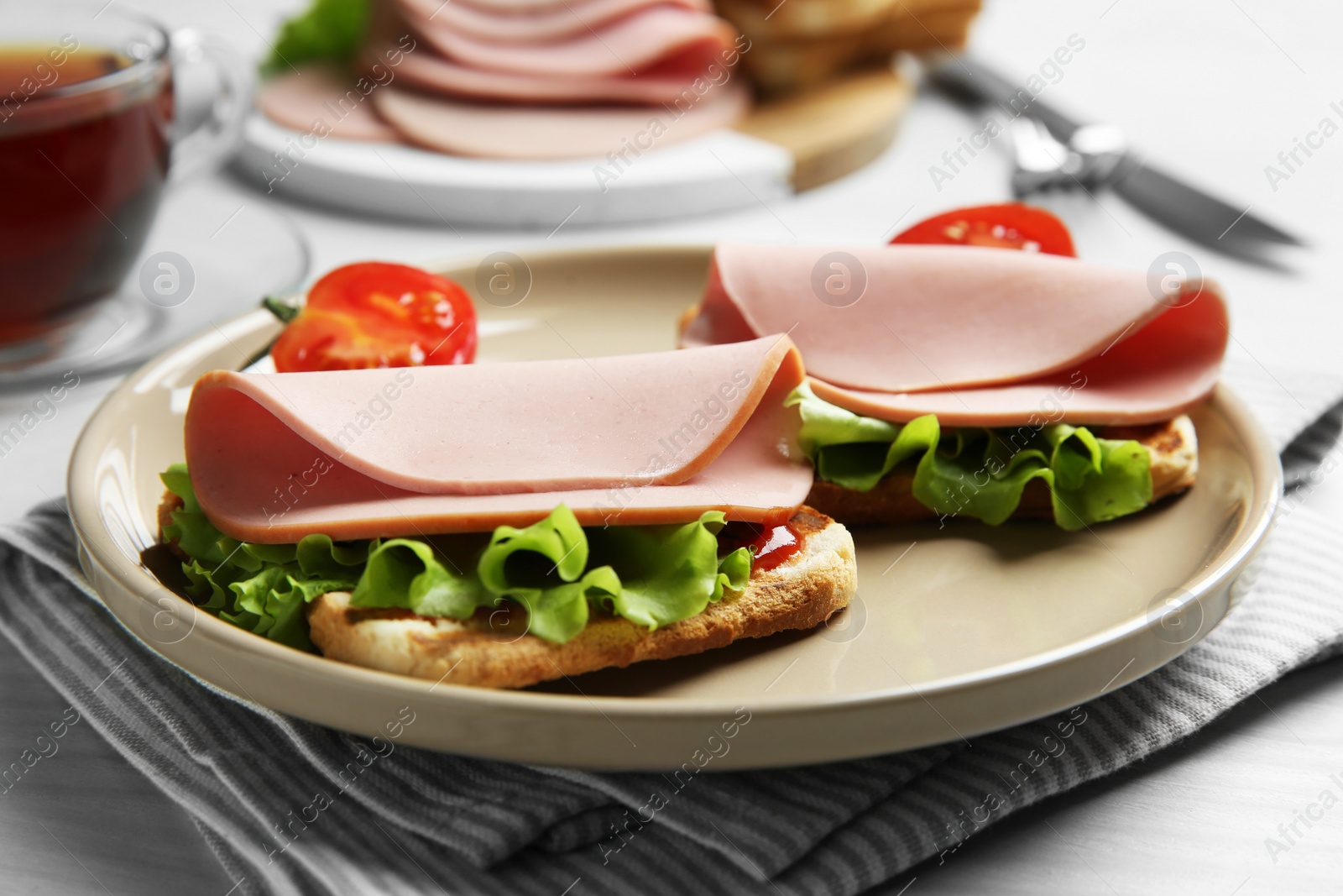 Photo of Plate of tasty sandwiches with boiled sausage, tomato and lettuce on white wooden table, closeup